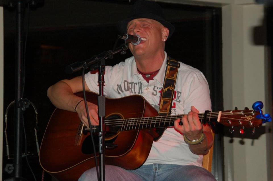 Photo of Steven John Rindt playing guitar and singing into a microphone