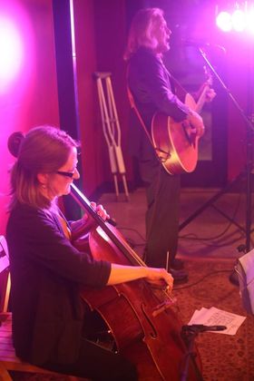 Photo of Todd on guitar and Angie on cello, performing music together on stage.